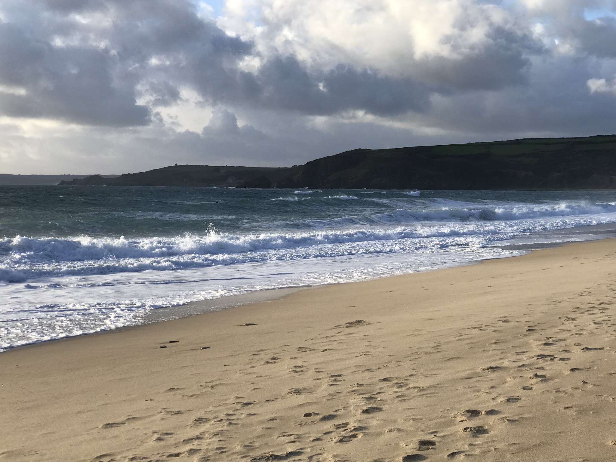 A sandy beach with rolling waves and a green headland