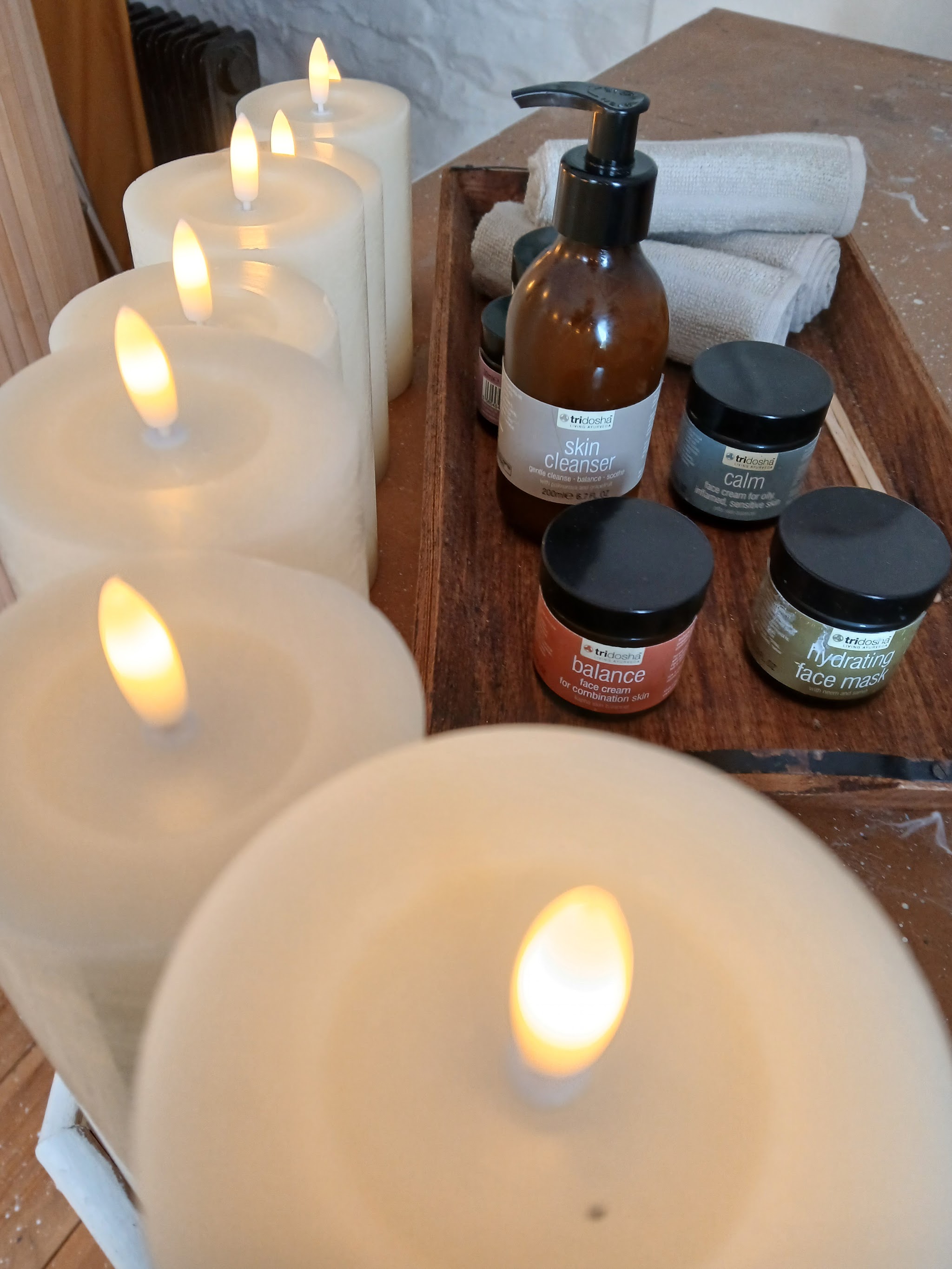 A row of glowing pillar candles beside oils and towels on a wooden tray