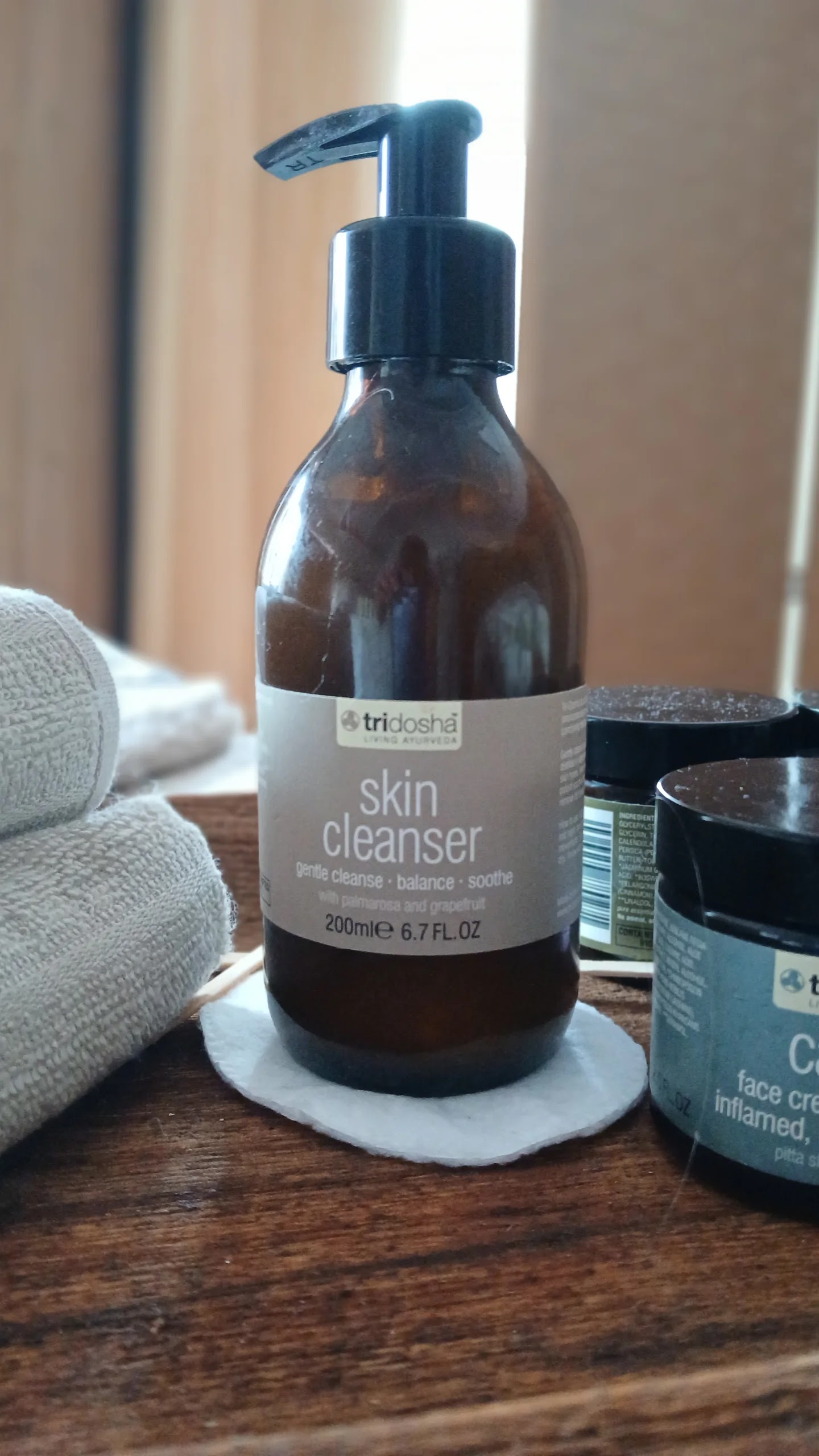 A bottle of skin cleanser and face cream jars on a wooden tray