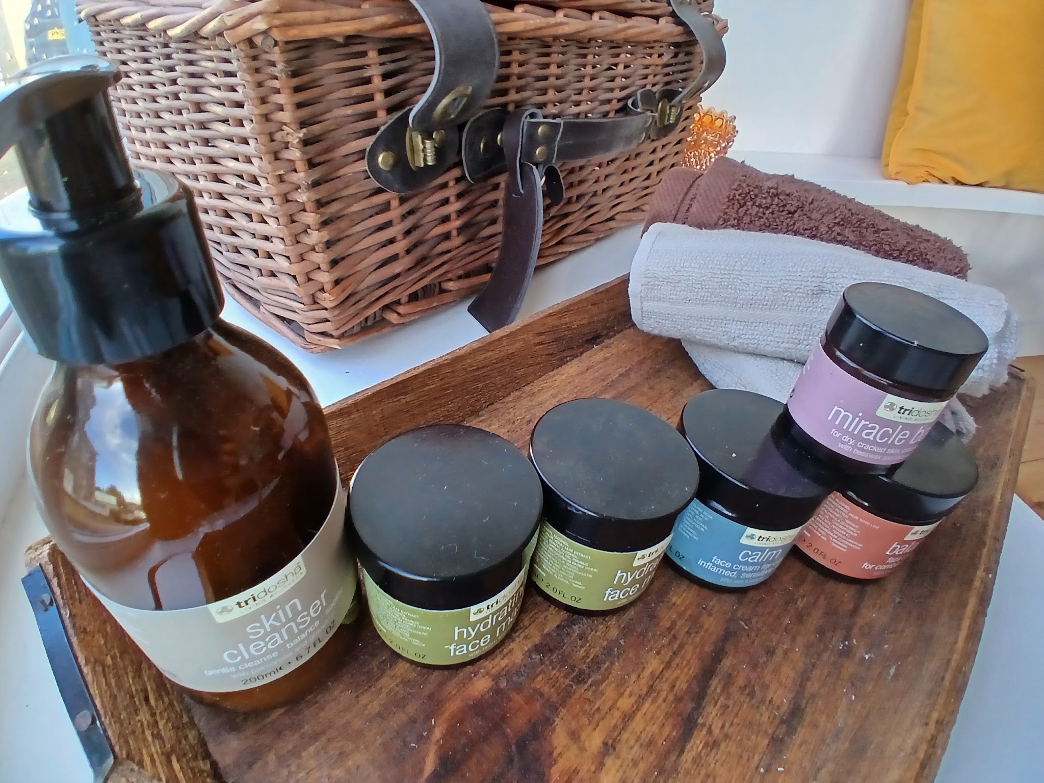 Oils and colourful jars of cream on a wooden tray, a wicker hamper behind
