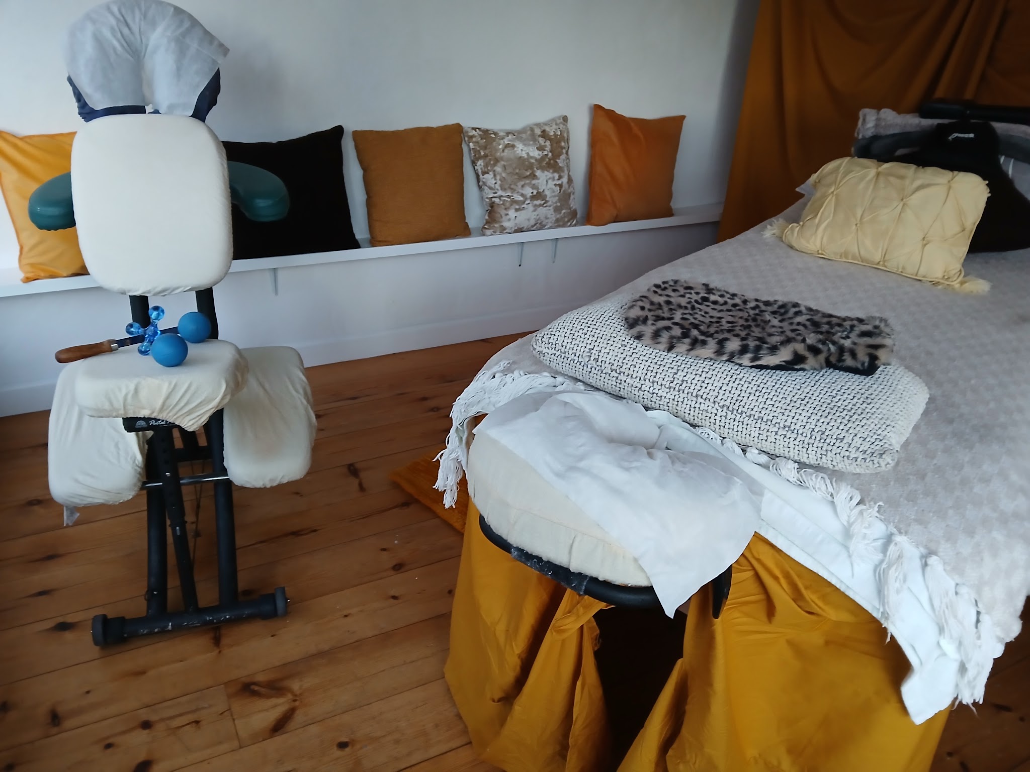 The treatment room with the massage chair beside the couch, cushions on the window seat and a wooden floor