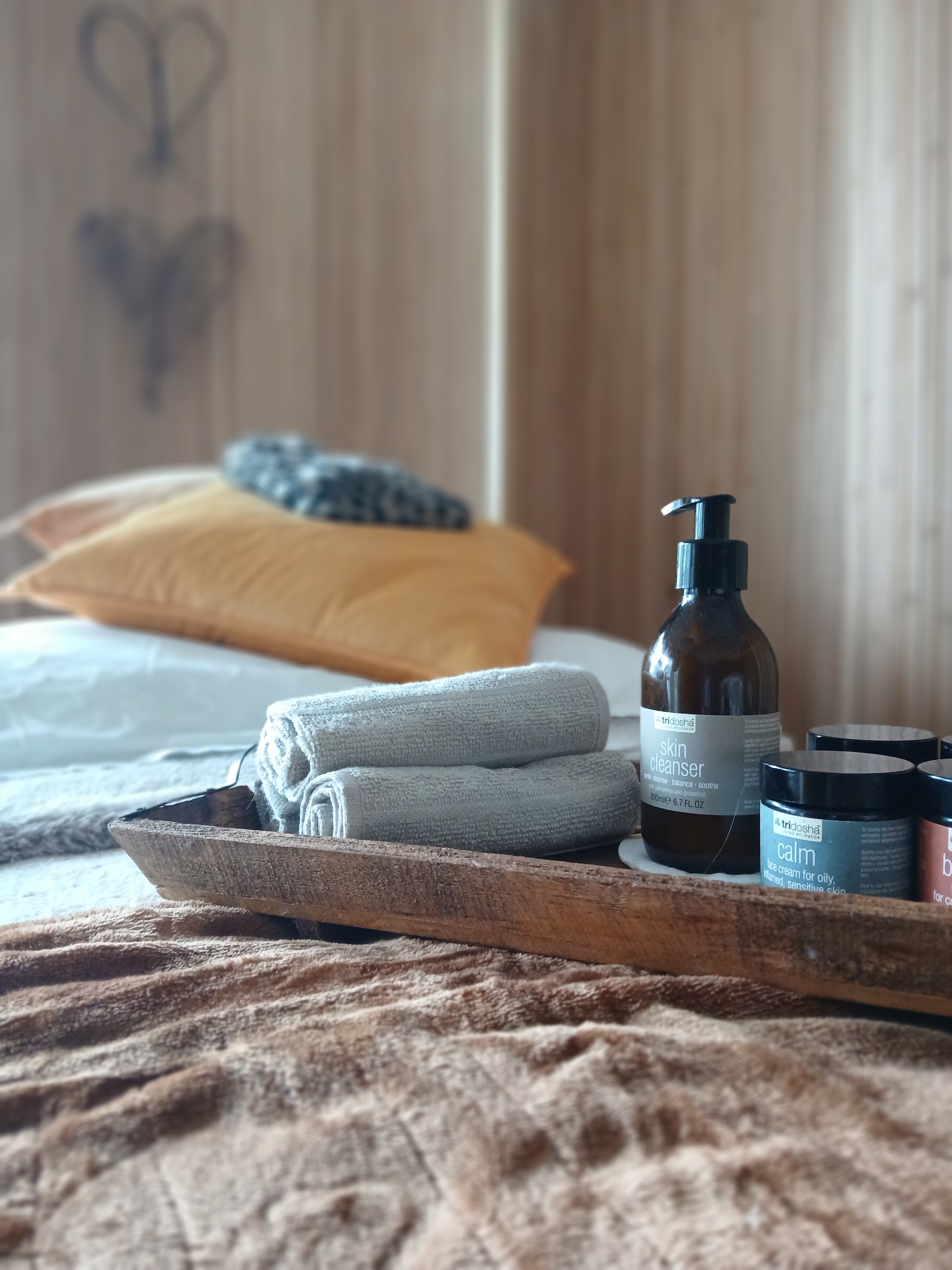 Rolled towels, oils and creams on a wooden tray on the couch, a willow heart on the screen behind