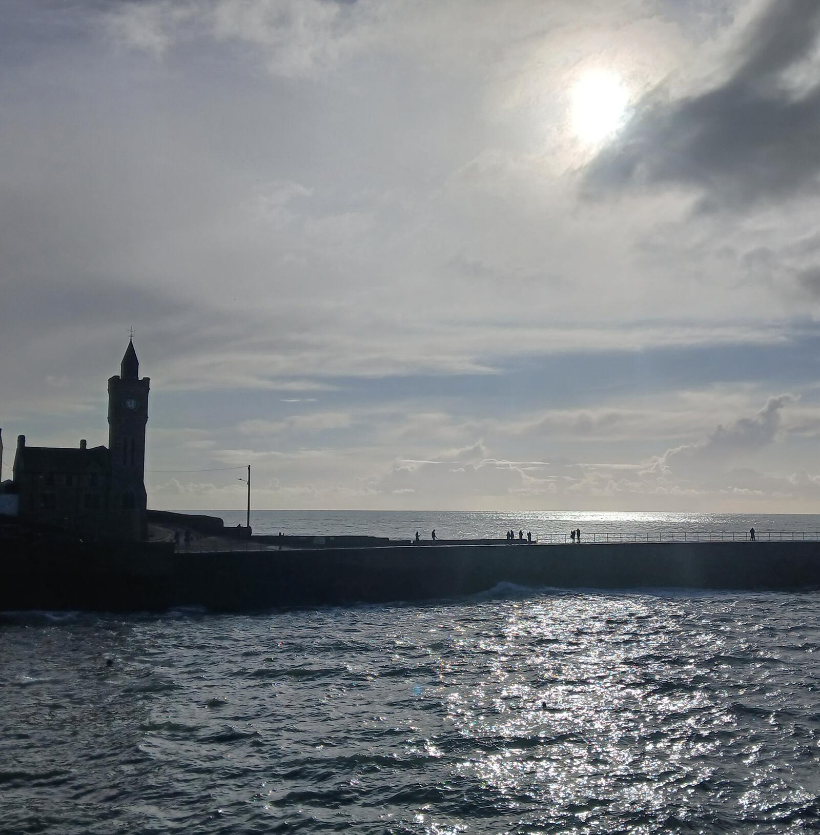 The Porthleven clock tower and harbour wall against a silver sea